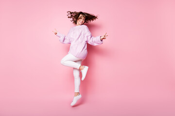 Full length body size view of pretty cheerful wavy-haired girl jumping showing v-sign isolated on pink pastel color background
