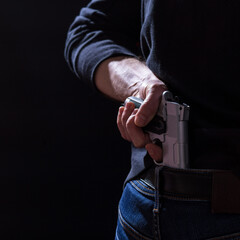 With a gun behind his back. Weapons legalization. Armed crime. The pistol is in the belt. Ready to use weapons.