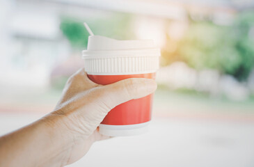 hot coffee cup in human's hand for take away,  with blurred garden background with copy space