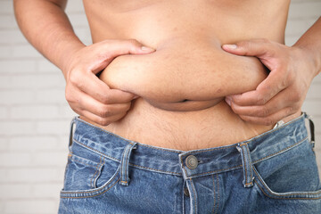 Naklejka premium man's hand holding excessive belly fat, overweight concept