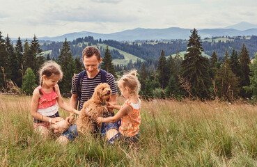 Dad with two little daughters and a dog on a glade on a background of mountains. Family with a...