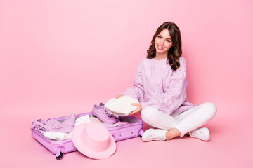 Obraz na płótnie Canvas Portrait of lovely cheerful girl packing valise folding clothes things tour preparation isolated on pink pastel color background