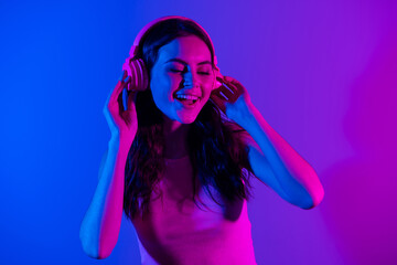 Photo of young smiling excited beautiful gorgeous girl listening music in headphones isolated on blue neon color background