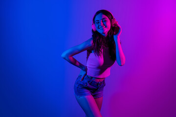 Photo of happy cheerful smiling beautiful girl dancing in headphones enjoying party disco isolated on glowing blue color background