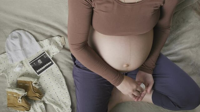 pregnant woman sitting on bed, pouring out pills from bottle on palm, top view