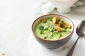 Summer cream soup with green fresh pea shoots. Top view. Green vegetable cream soup in a white bowl on a gray concrete background top view. Vegan soup puree of green vegetables. Vegetarian and diet fo