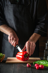 Close-up of a chef hands cutting peppers on cutting board. Professional preparation of salad in the kitchen in a restaurant or cafe. Vertical image