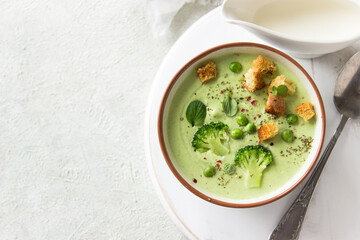 Summer cream soup with green fresh pea shoots. Top view. Green vegetable cream soup in a white bowl on a gray concrete background top view. Vegan soup puree of green vegetables. Vegetarian and diet fo