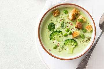 Summer cream soup with green fresh pea shoots. Top view. Green vegetable cream soup in a white bowl on a gray concrete background top view. Vegan soup puree of green vegetables. Vegetarian and diet fo