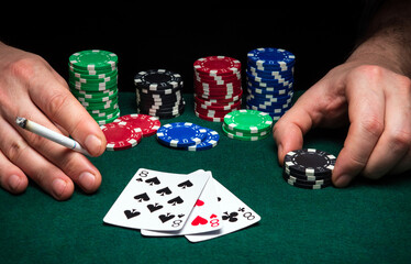 Hands of a gambler closeup and chips on green table in a poker club. A player places a bet on winning poker  three of a kind or set combination