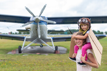 A Caucasian woman and her little daughter are playing a pilot against the backdrop of a small plane...