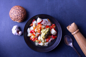 Diet soup in a black plate, round bread, garlic, pepper, spoon on a blue background. Healthy food concept. Flat lay.