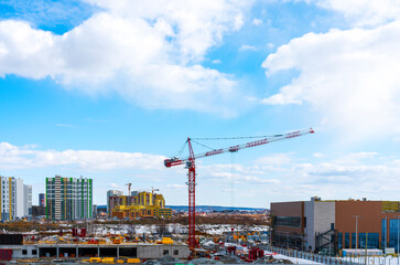 Construction of a new multistory building in the city, red construction crane on a blue cloudy sky...