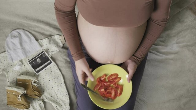 Top vew of expecting pregnant woman with large belly eating tomatoes at home