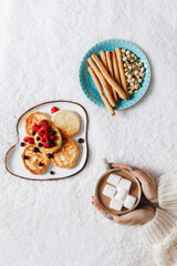 Woman holding a cup with marshmallows on background with cheesecakes and snacks. Flat lay. Lunch concept
