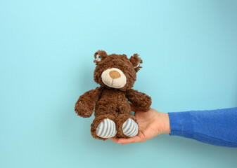 female hand hold a small brown toy teddy bear