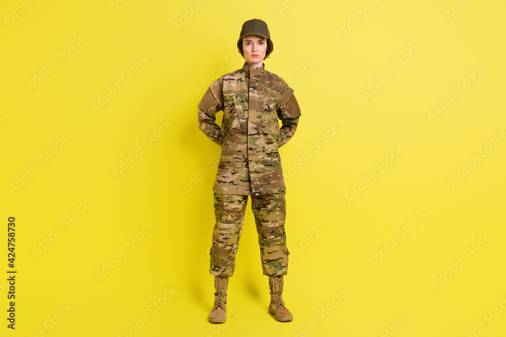 Wall mural Full size photo of concentrated young girl standing arms behind back isolated on yellow color background