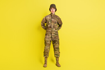 Full size photo of concentrated young girl standing arms behind back isolated on yellow color background