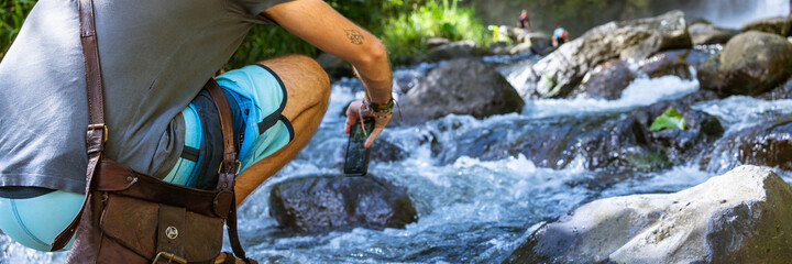 Person next to a river taking a picture of a waterfall