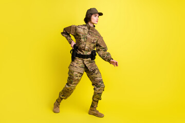 Full body profile portrait of pretty military girl look empty space arm on pistol isolated on yellow color background