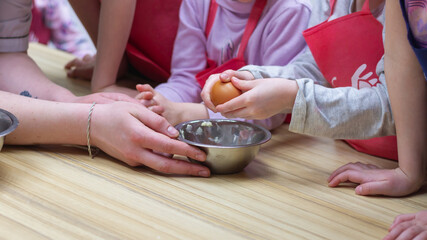 Obraz na płótnie Canvas Children learn to cook and break an egg into a bowl