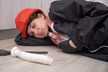 a drunken plumber in uniform and hard hat sleeps on the floor, with tools and an empty bottle scattered nearby. Alcohol addiction at work