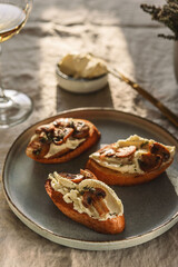 Bruschettas or toasts with cheese and fried mushrooms with thyme served with glasses of wine on greige linen tablecloth