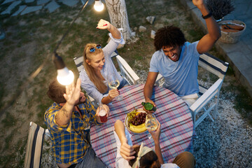 top view of multiethnic group of friends gathered, socializing, talking, laughing, sitting at the table with hands up