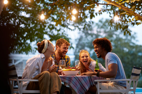 group of multiethnic friends laughing, gathered, talking, sitting at the outdoor table