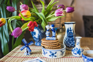 Breakfast in spring with Dutch cookies stroopwafels and fresh tulips. Figurines of kissing boy and girl and windmill.
