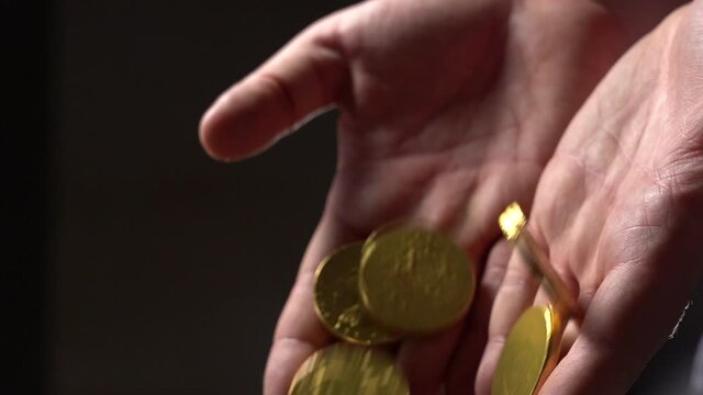 Gold Coins fall from the man's palms. Hands with gold coins on a black background. Slow motion. Close Up.