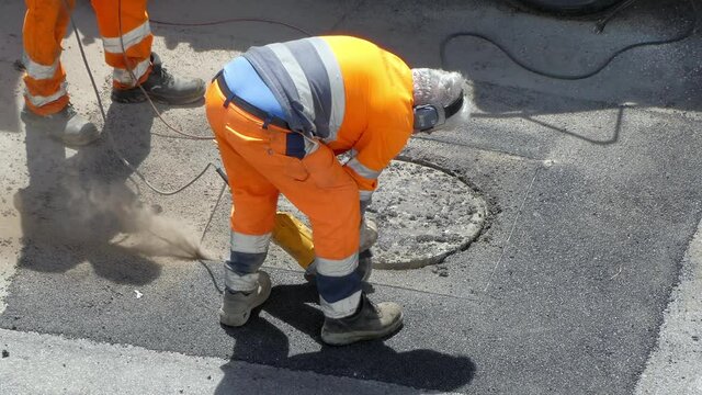 Men in protective uniform working on construction site outdoors, road workers cutting round shape cement on sidewalk with cutting tools, manual workers drilling asphalt for hydraulic repairing