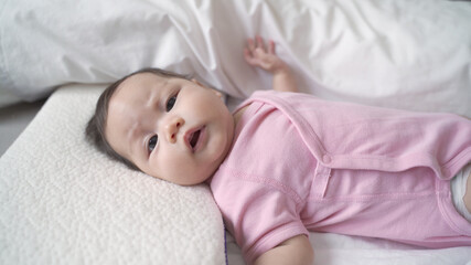 Fototapeta na wymiar asian baby infant laying down on white soft bed feeling hungry. 3 months old baby facial expression. sign and symptom of hungry in kid.
