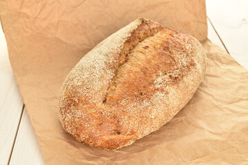 One fresh loaf of bread on craft paper, close-up, on a wooden table.