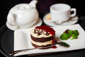 Dessert with white and black sponge cake on a white plate with a tea cup and teapot. Close-up, selective focus