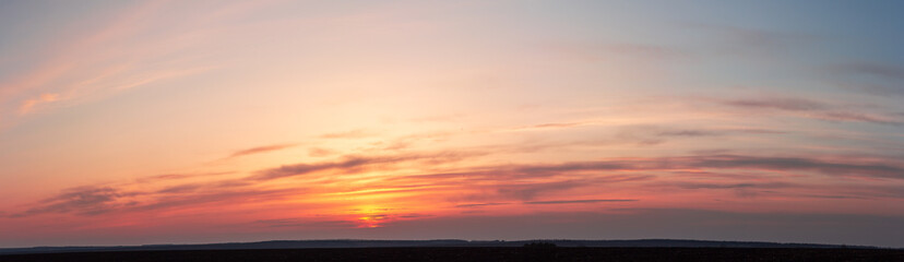 Obraz premium Panorama of red sunset. The yellow sun disappeared behind striped clouds