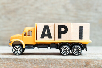 Toy truck hold alphabet letter block in word API (Abbreviation of Application programming interface or Active pharmaceutical ingredient) on wood background