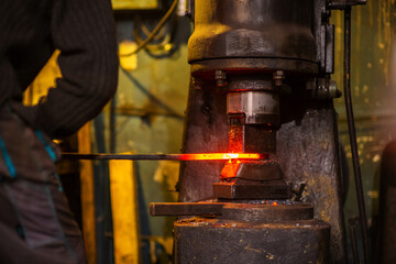 A blacksmith forging a red-hot iron billet on an automatic wall. Handicraft concept