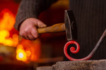 Close-up of the hands of a blacksmith twisting a spiral with a hammer, putting a red-hot iron blank on an anvil. Work in the forge