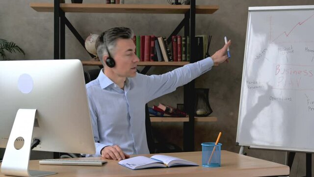 Serious influential intelligent caucasian middle aged ceo, manager or business mentor, conducts online briefing for coworkers via video conference, shows a presentation, business plan on a flipchart