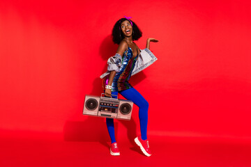 Obraz na płótnie Canvas Photo of charming cute wavy dark skin lady wear pin up outfit holding boombox looking empty space isolated red color background