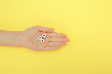 A woman's hand holds three dice. A game of dice with numbers. Board game items. yellow background.