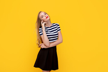 Shy girl smiling looking to the camera. Caucasian charming girl with long hair wearing stripped t-shirt, standing against yellow studio background having fun