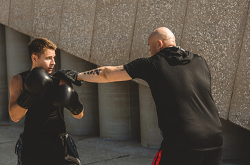 Two men exercising and fighting in outside. Boxer in gloves is training with a coach