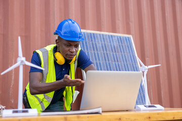 African american engineer and caucasian electrician wearing blue hard hat working on laptop computer