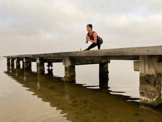 Fototapeta premium Young woman practices yoga on a lake with cloudy sky