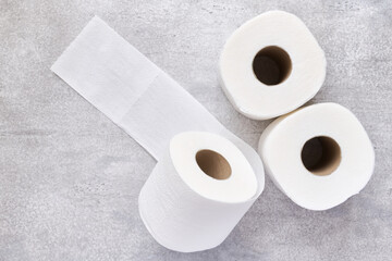 Three white rolls of toilet paper on a gray concrete background, shallow depth of field