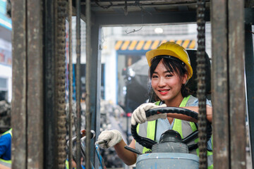 Industrial worker woman wearing helmet driving forklift car at manufacturing plant factory industry, Asian beautiful female engineer and many engine parts as blurred background