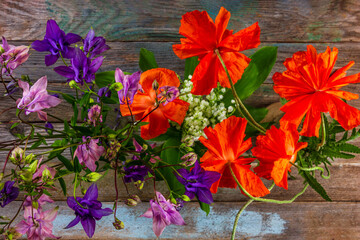bouquets of aquilegia flowers and red poppies on a wooden background close-up top view