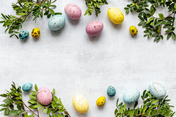 Layout of colorful Easter eggs with spring branches and green leaves, top view